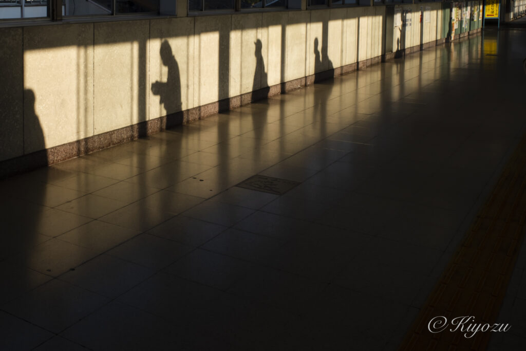 駅に通路にあたる西日に寄ってできる影。人々のシルエット。