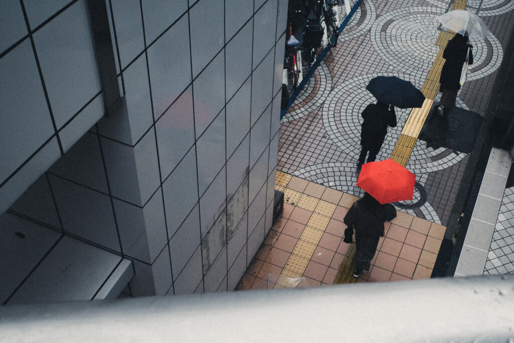 歩道橋の上から、赤い傘の人を見下ろしたストリート写真