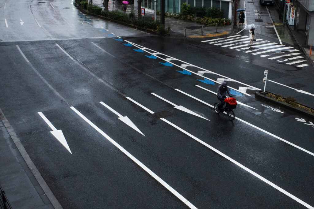 雨の広い道を走る１台の自転車の写真