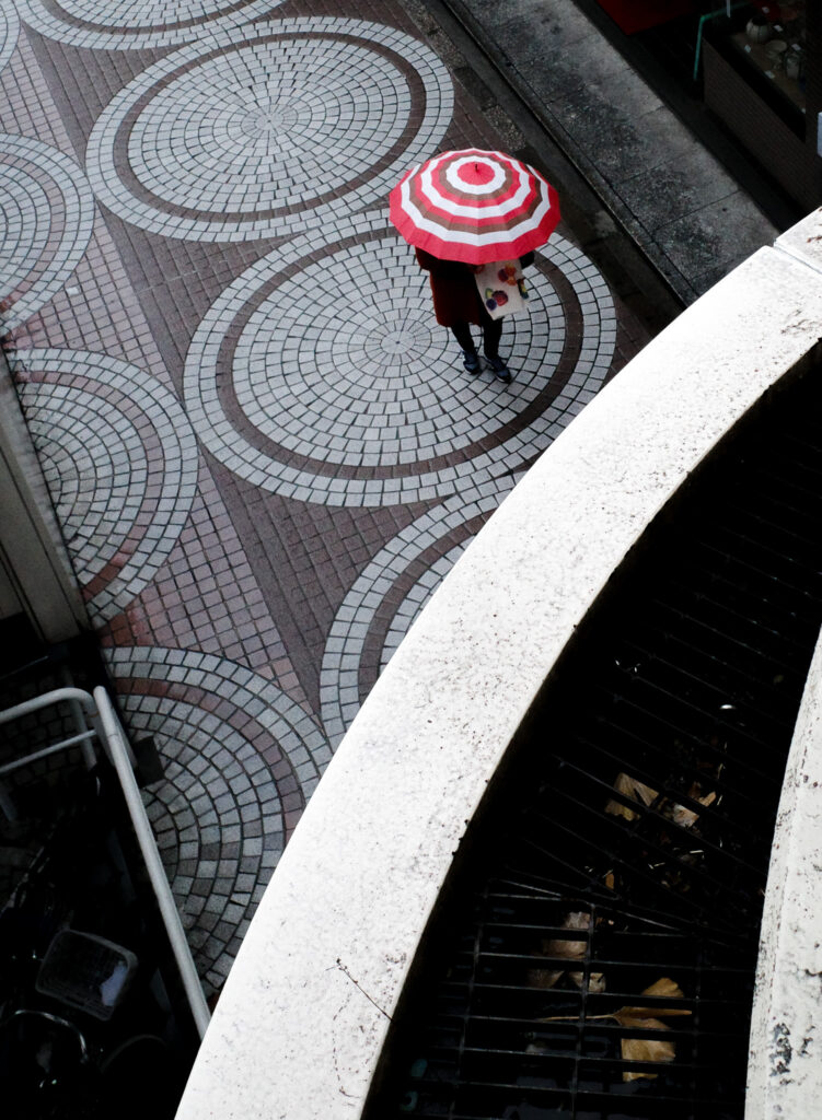 路面の円形タイルと、円状の傘を刺した人のストリート写真