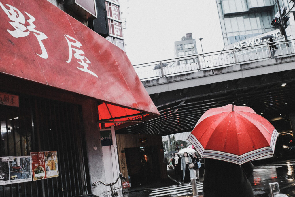 赤い店先の看板と、赤い傘を刺した女性のストリート写真