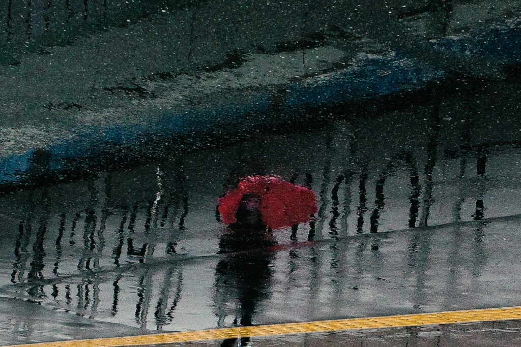 路面の水たまりに映る、赤い傘の女性