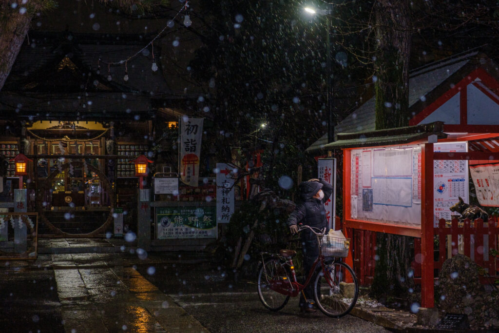 雪の中で神社の掲示を見る人